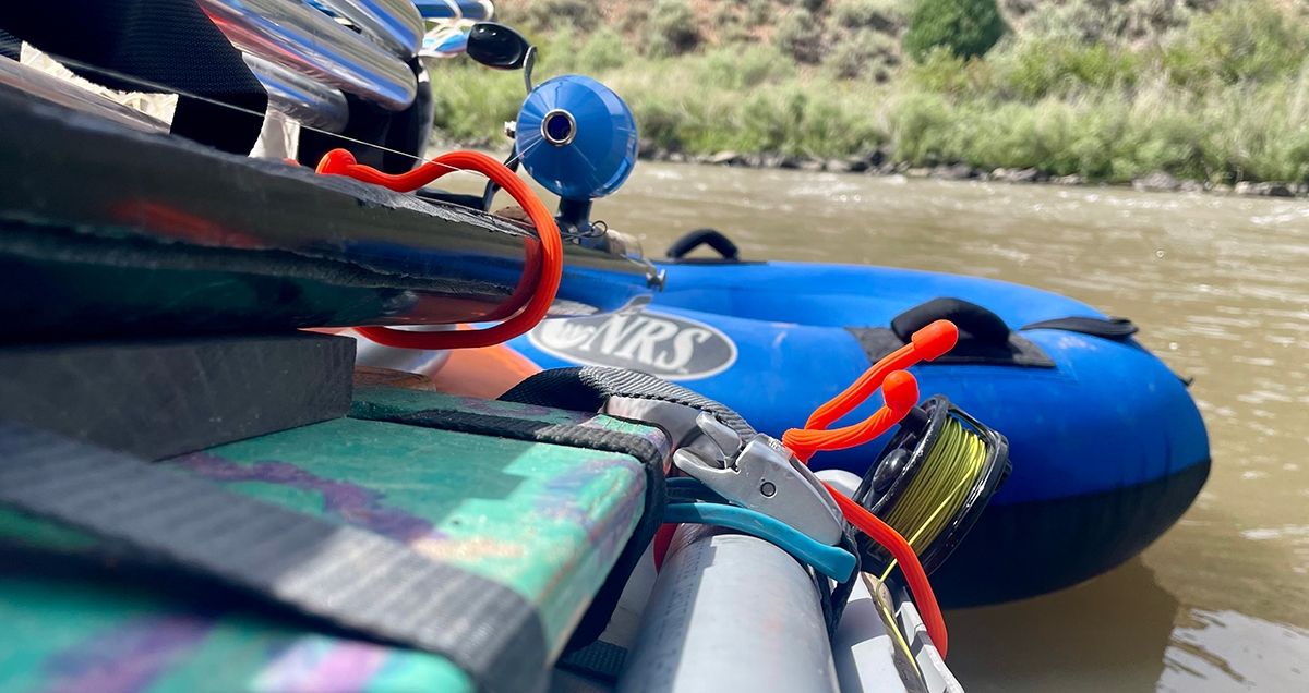 A close up image of river raft with a tie down strap holding down gear and gear ties holding down fishing rods
