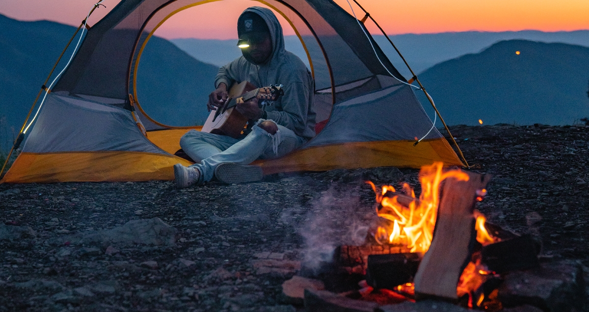 Man playing guitar in a camping tent in front of a campfire