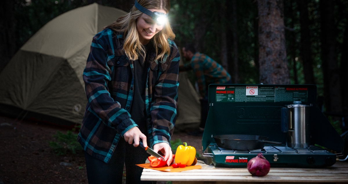 Woman wearing a Radiant headlamp while cooking at a campsite