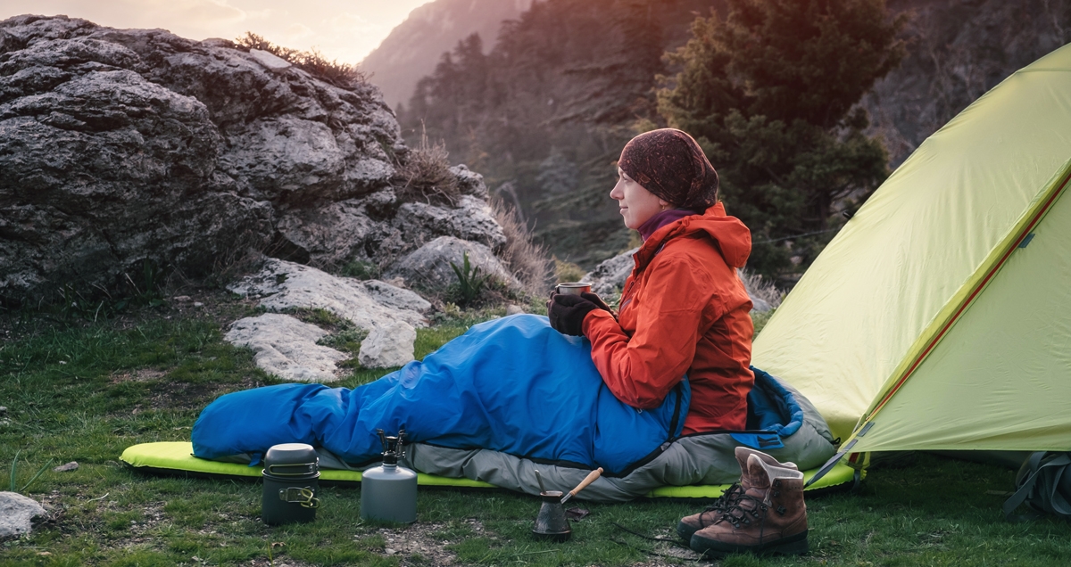 Woman in sleeping bag beside camping tent